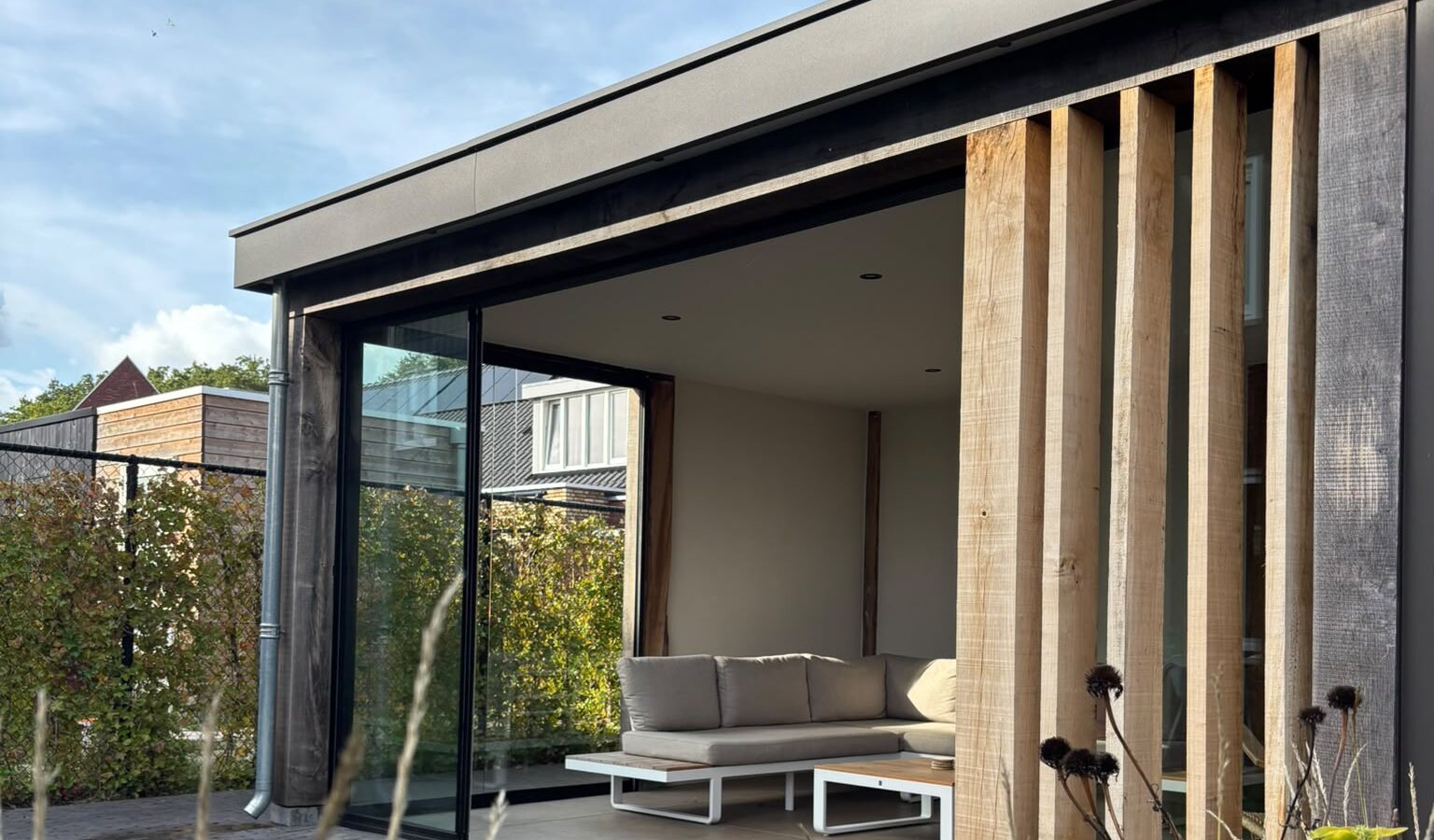 Tuinkamer in Harskamp met eiken lamellen, een glazen schuifwand en een loungebank.