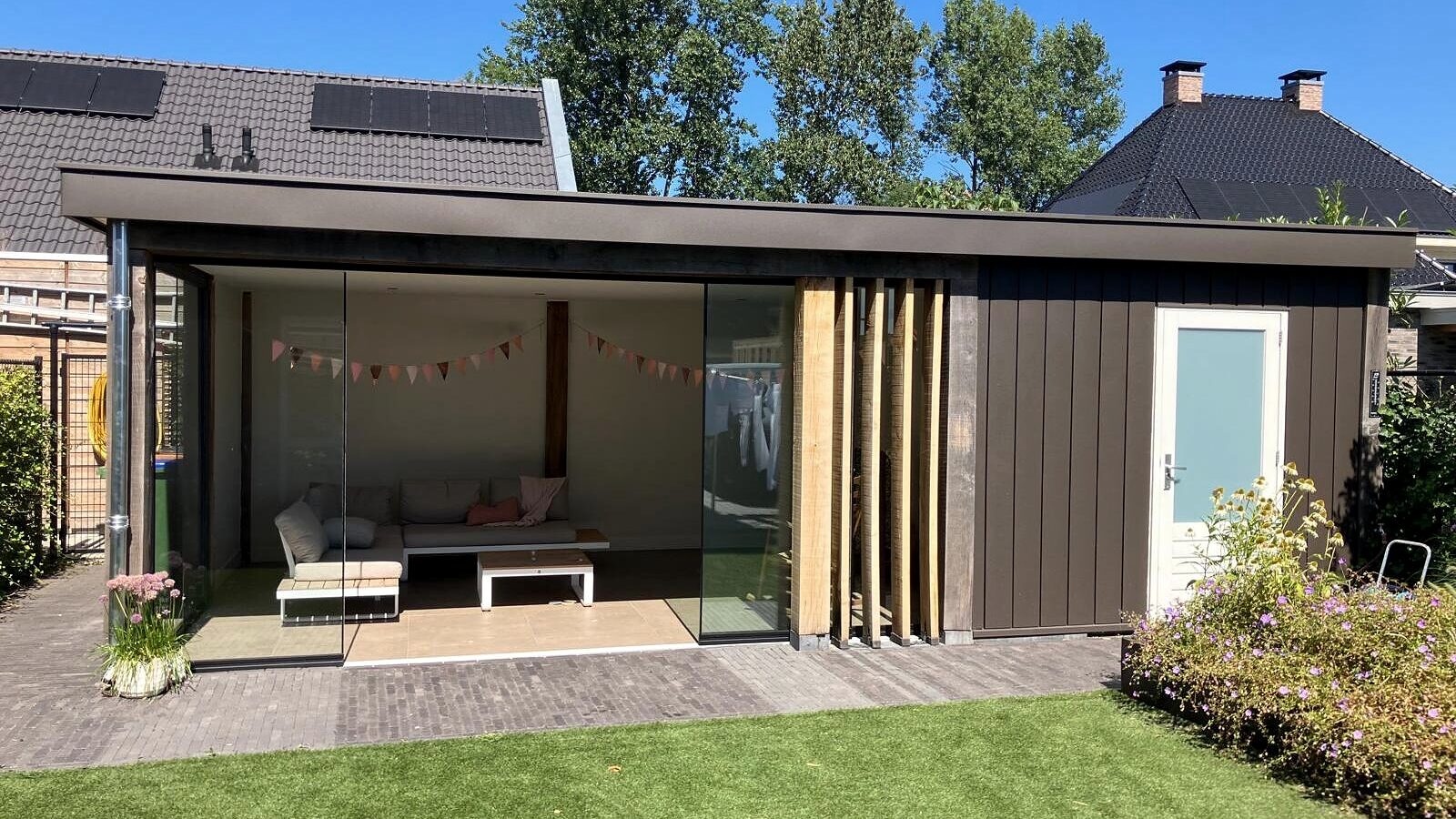 Tuinkamer met berging in Harskamp, met glazen schuifwand en strakke verticale lamellen.