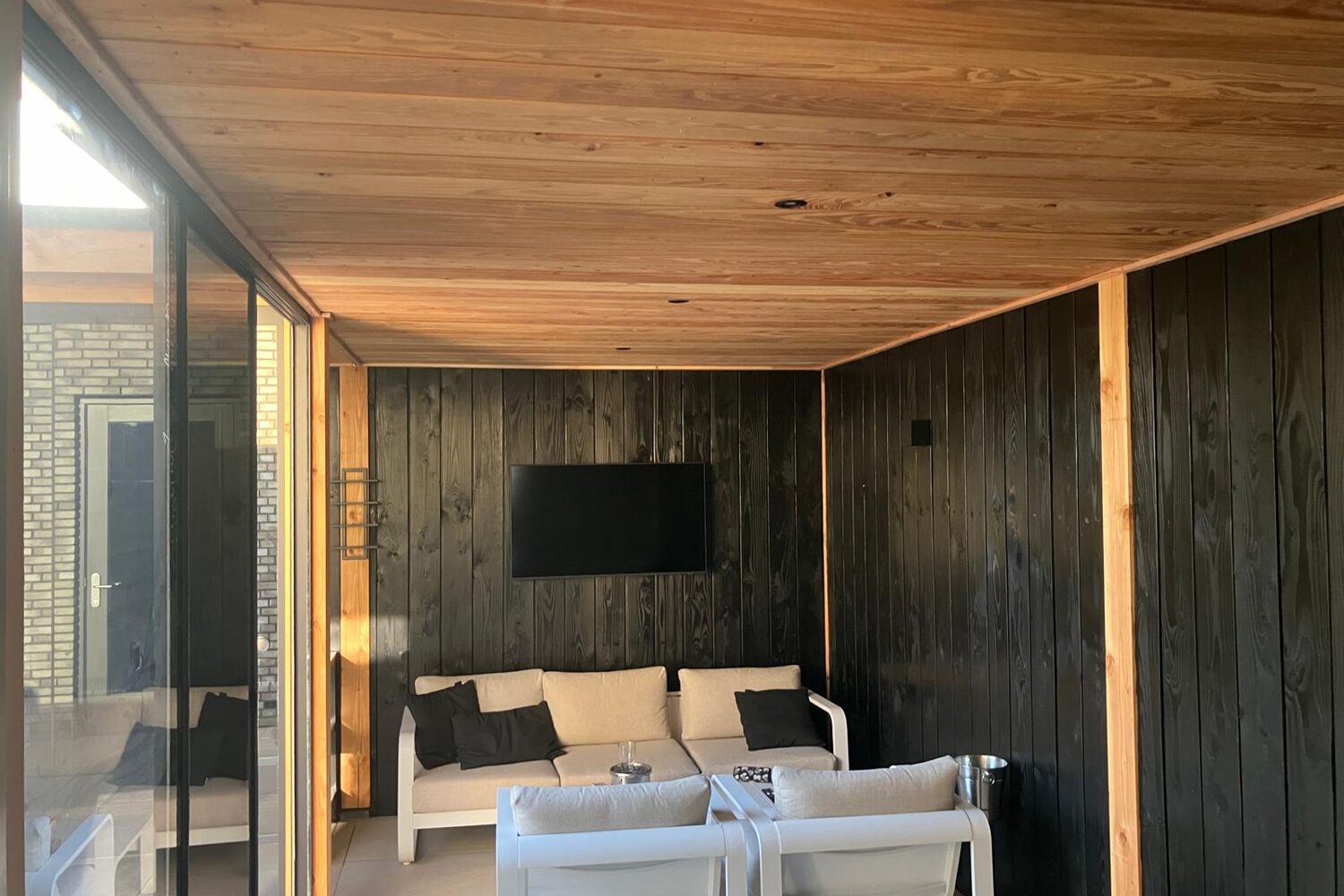 Interieur van een tuinkamer met een douglas plafond en zwarte houten wanden.