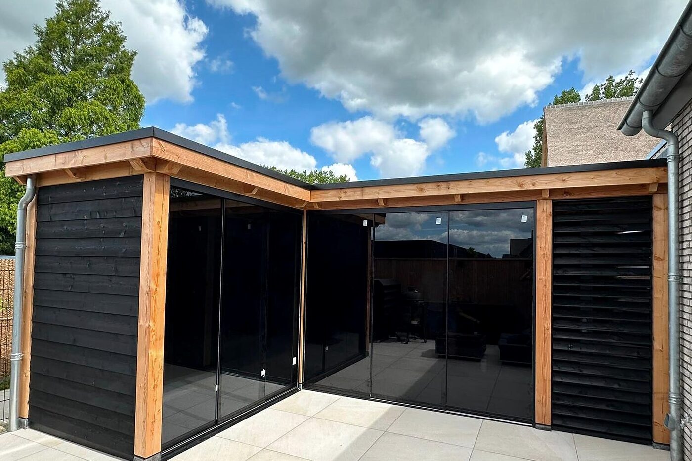 L-vormige tuinkamer in Nijkerk met zwarte gevelbekleding, glazen schuifwanden en douglas stijlen.